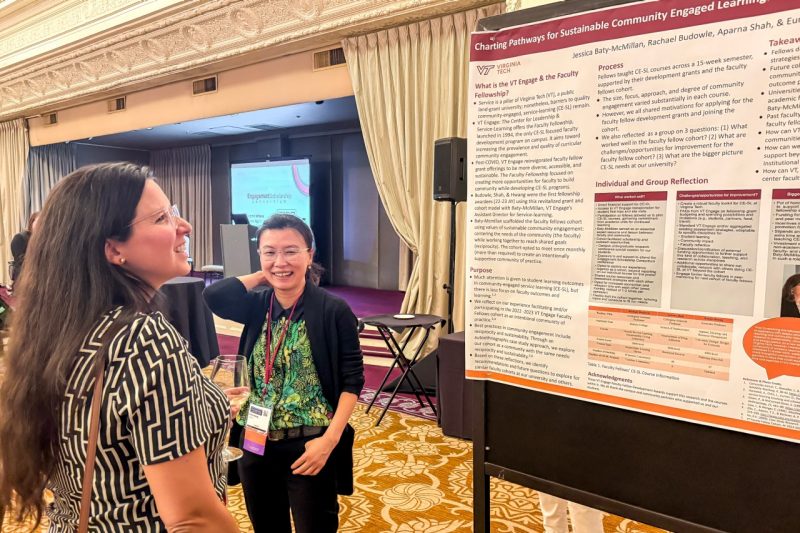 Two women laugh as they look up at a poster filled with text.